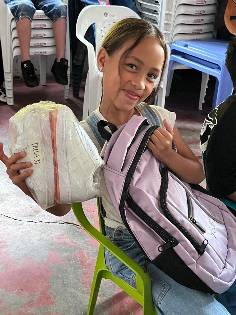 Niña sonriente con una donación de útiles y calzado
